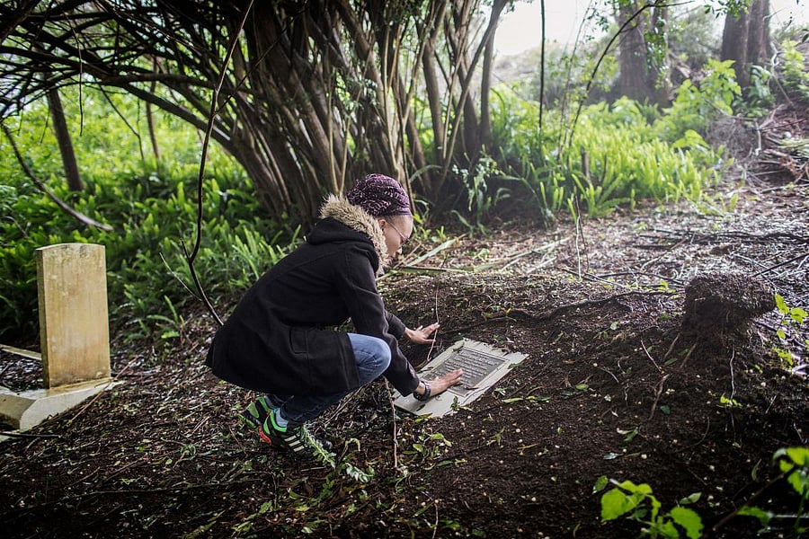 (FILES) This file photo taken on October 18, 2017 shows environmental manager of Basil Read construction firm, Namibian born Annina Van Neel Hayes, paying her respects over a plaque commemorating the burial place of the remains of some liberated African slaves found during the construction of a power plant, at the graveyard of Saint Paul's Cathedral, south of Jamestown, in the British Overseas Territory of Saint Helena. Nine years ago skeletons of 325 former slaves were discovered during the construction of St. Helena's first airport on the South Atlantic island. After it abolished slave trade in 1807, Britain intercepted Portuguese slave ships sailing off the waters of St. Helena - which lies on what was then a notorious slave route from Africa to the Americas. Between 1840 and 1865, around 25,000 slaves were freed and released on St. Helena, according to historians. / AFP PHOTO / GIANLUIGI GUERCIA