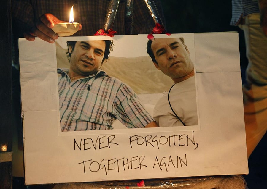 A member of the Pakistani media holds a clay-lamp next to a picture of slain Agence France-Presse reporter Sardar Ahmad, left, who was killed in a 2014 attack on a hotel in Kabul, and Shah Marai, right, an AFP photographer killed in Monday's suicide bombing in Kabul, during a vigil Tuesday, May 1, 2018, in Islamabad, Pakistan. AP/PTI