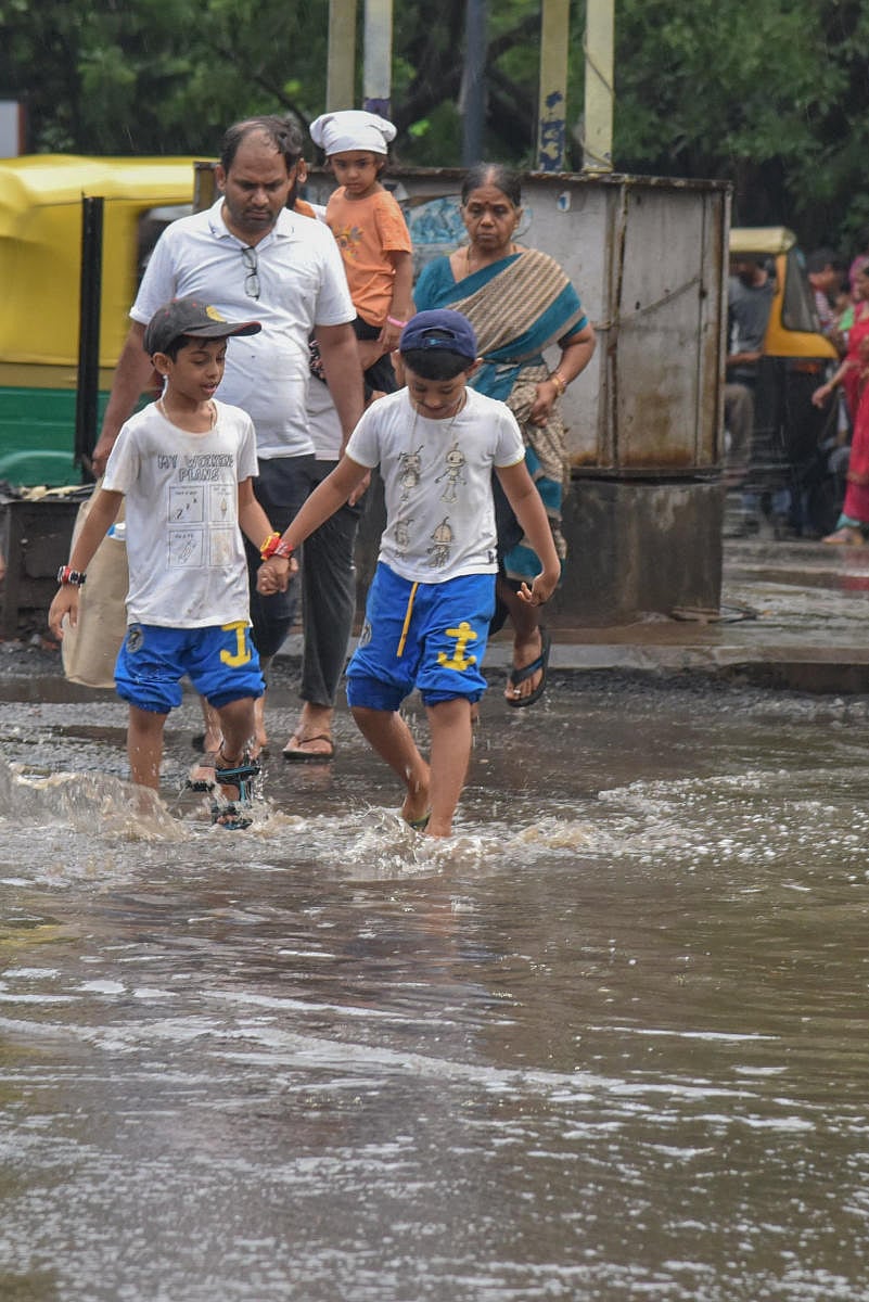 People laboriously cross the road in rain water at MG statue circle in Bengaluru on Sunday. Photo by S K Dinesh