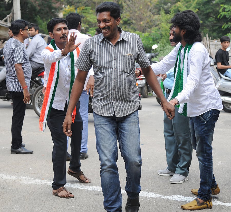 A voter is amused as workers of both the Congress and the JD(S) beseech him to vote for their party in Rajarajeshwari Nagar on Monday. DH PHOTO/SRIKANTA SHARMA R