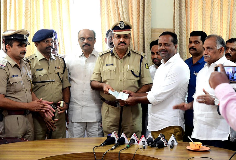 District In-charge Minister U T Khader hands over a cheque for Rs 1 lakh as a reward for Panambur police, to City Police Commissioner T R Suresh, in Mangaluru on Friday.