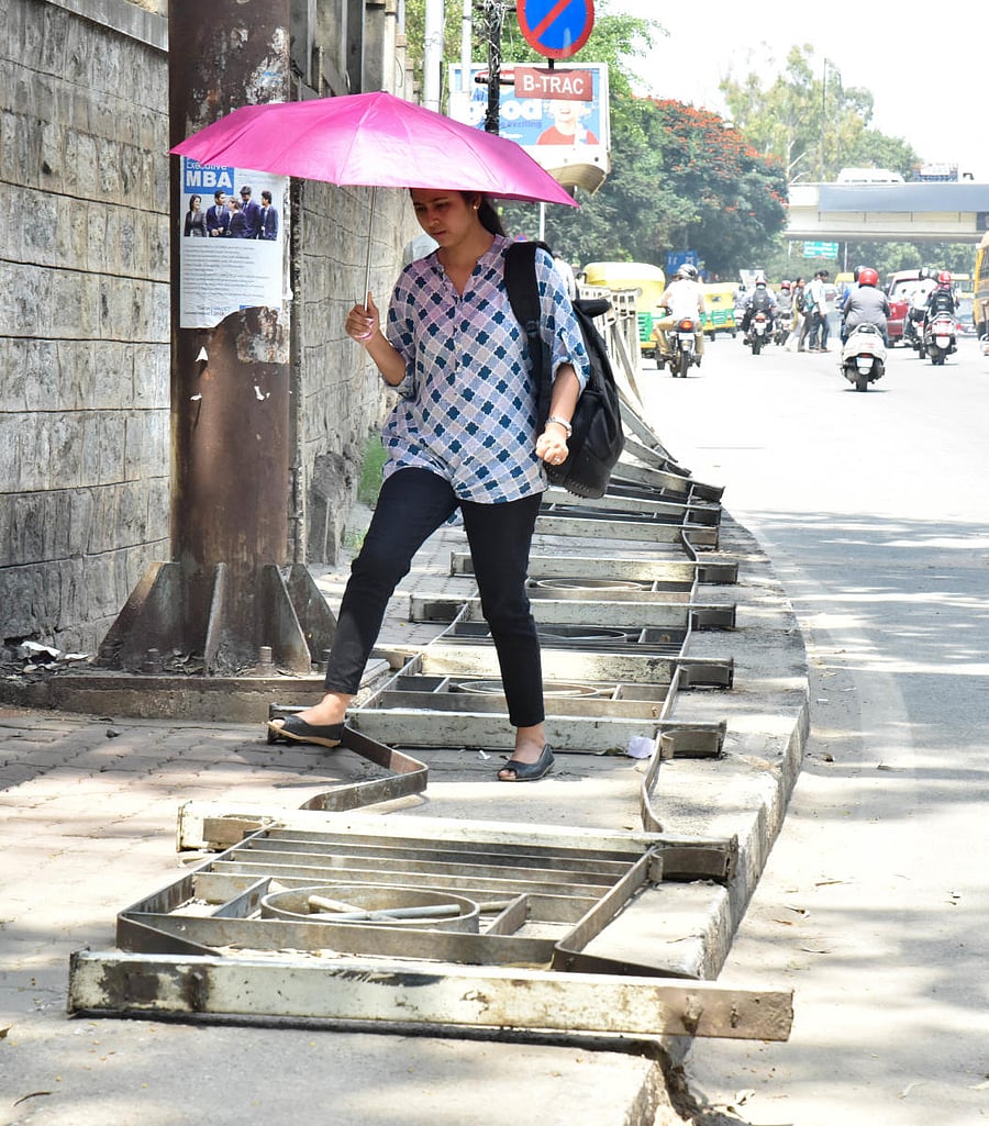 A pedestrian struggling to free walk while the barricade fell on footpath at Bannerghatta road in Bengaluru. DH Photo/Janardhan B K