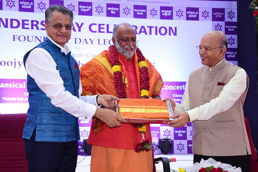 Corporate Guru Swami Sukhabodhananda, the main speaker at the Founders’ Day celebration of Karnataka Bank, is felicitated by Bank Managing Director and CEO Mahabaleshwara M S and Chairman P Jayaram Bhat at the bank’s head office in Mangaluru on Monday.