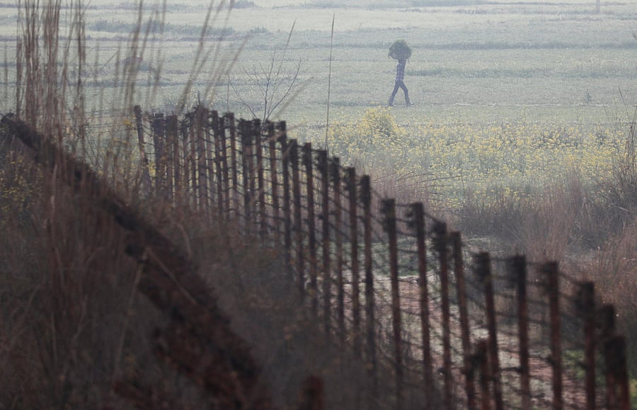 A farmer carries a sack of grass as he walks near the fenced border between India-Pakistan in Ranbir Singh Pura sector near Jammu March 1, 2019. REUTERS/Adnan Abidi
