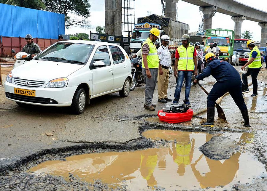 Civil Defence volunteers clearing rain water that had collected in potholes near R V College of Engineering on Mysuru Road on Sunday. DH Photo