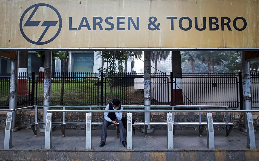 FILE PHOTO: A man waits at a bus-stop with an advertisement of Larsen &amp; Toubro outside the company's manufacturing unit in Mumbai. REUTERS