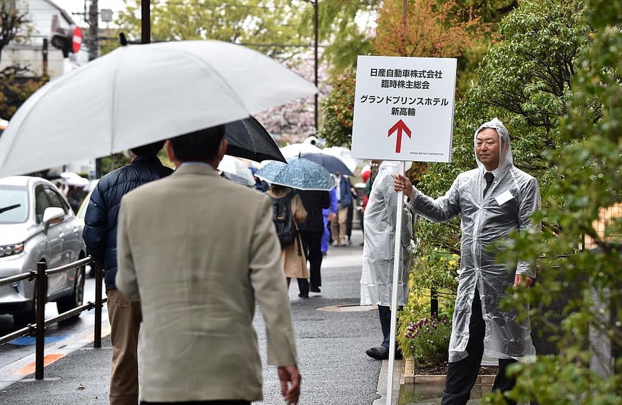 A Nissan Motor employee holds signage on a sidewalk to guide arriving shareholders to a hotel where the company's extraordinary shareholders' meeting will take place in Tokyo on April 8, 2019. AFP
