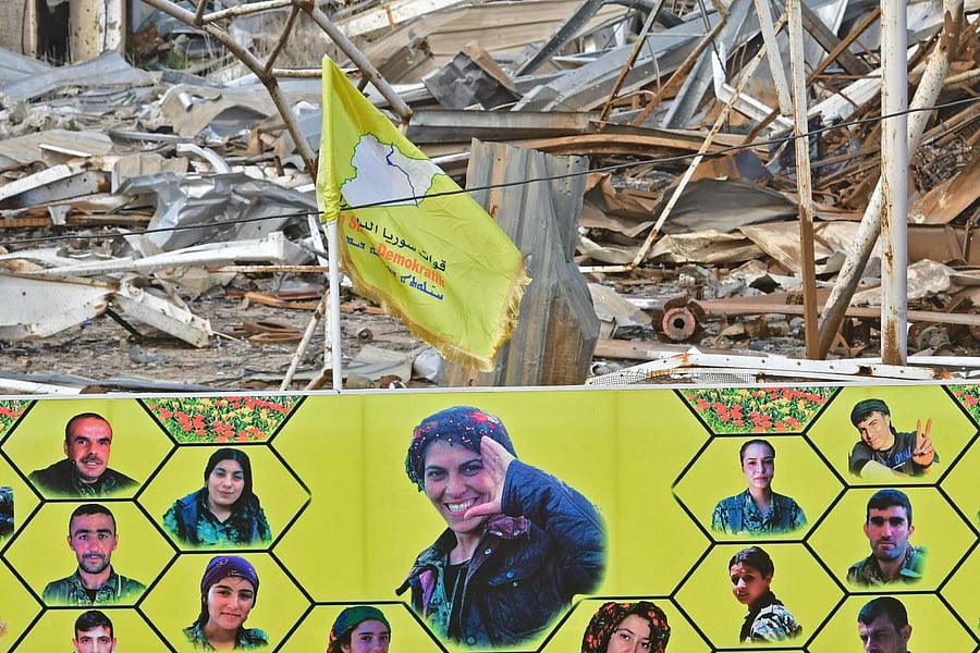 A woman stands by a large banner showing the faces of fighters of the US-backed Kurdish-led Syrian Democratic Forces (SDF), who were killed during battles with the Islamic State (IS) group, near the Omar oil field in the eastern Syrian Deir Ezzor province