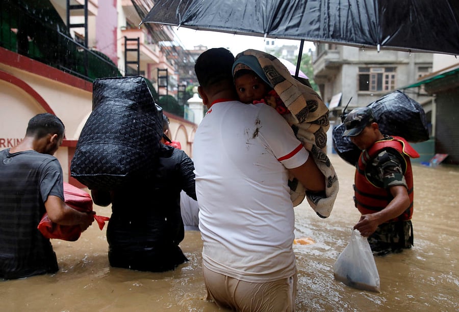 A man carrying a child walks towards the dry ground from a flooded colony in Kathmandu, Nepal July 12, 2019. REUTERS