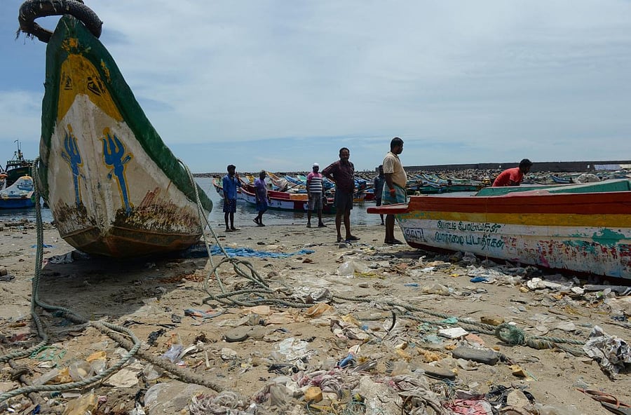 Fishermen walk past garbage dumped on a beach at a fishing harbour in Chennai on May 10, 2018. / AFP PHOTO