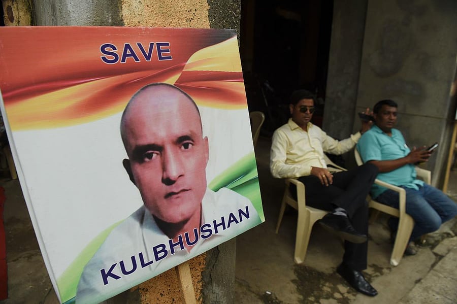 Indian residents sit next to a placard with the picture of Kulbhushan Jadhav, an Indian national convicted of spying in Pakistan, in the neighbourhood where he grew up, in Mumbai on July 17, 2019. (Photo by AFP)
