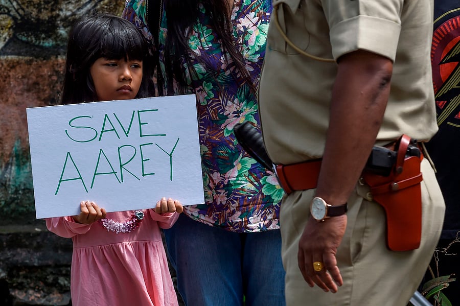 A policeman walks past a child holding a poster as she protests against the destruction of Aarey forest which they call "Mumbai's Amazon", after the government approved cutting down 2,700 trees for constructing a metro train car shed, in Mumbai. (AFP Photo)
