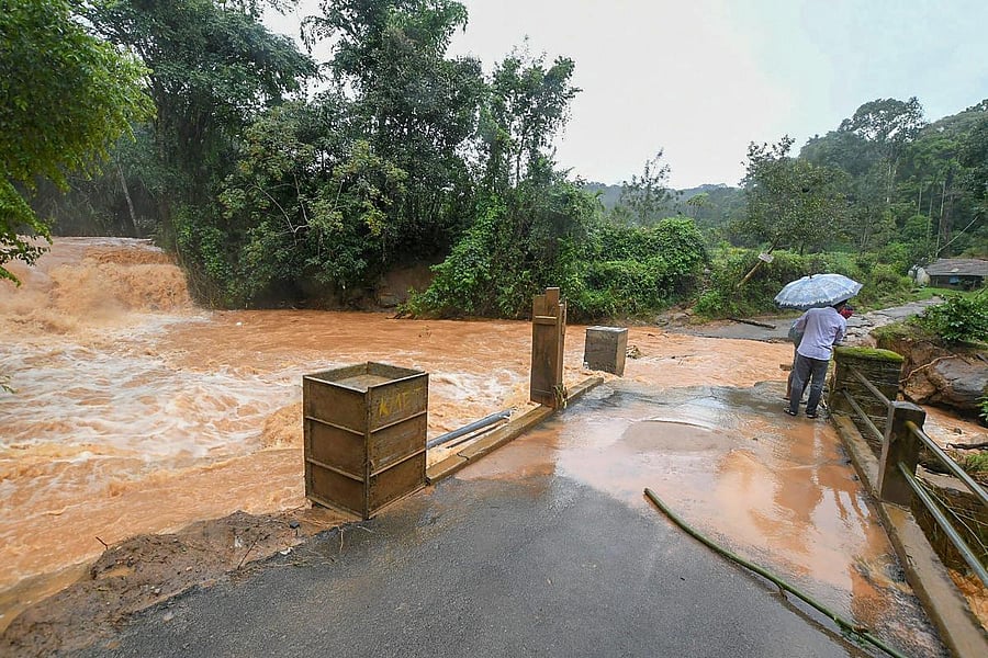 People walk across a bridge overflowing due to heavy monsoon rainfall, in Kodagu on Sunday, Aug 19, 2018. (PTI Photo)