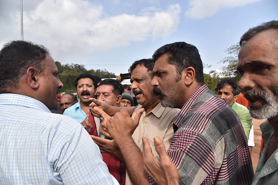 People confront Tahsildar Mahesh (extreme left) at Madapura bus stand in Somwarpet taluk to ensure food supply to rain victims.DH PHOTO / B H Shivakumar