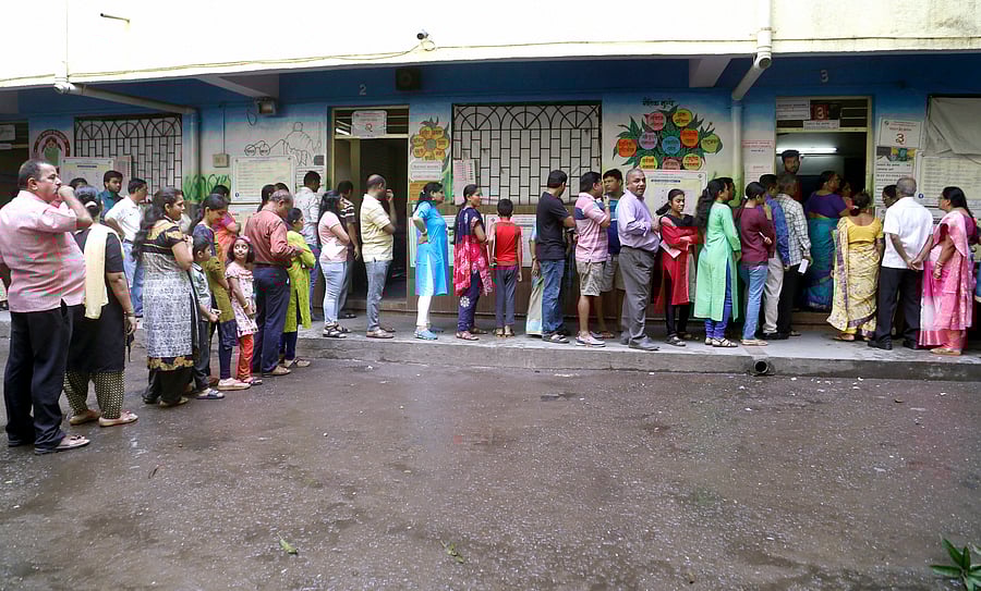 Voters stand in a queue displaying their voter card outside a polling station during Maharashtra Assembly elections, in Thane. (PTI Photo)