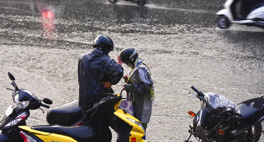 A woman is busy with her mobile phone as rain pounds JC Road, Bengaluru, on Friday. DH PHOTO/Chandrahas Kotekar