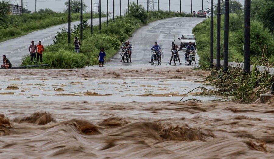 Onlookers and commuters stand next to a flooded water channel flowing over a bridge after heavy rains at New Chandigarh. (AFP photo)