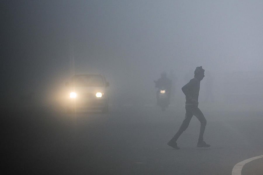 A man crosses a street as commuters make their way under heavy foggy conditions in New Delhi on December 30, 2019. (AFP Photo)