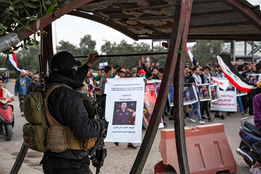 An Iraqi policeman stands guard as protesters march past during an anti-government demonstration, also calling for freedom of the press, in the southern Iraqi city of Basra on January 17, 2020. (AFP Photo)