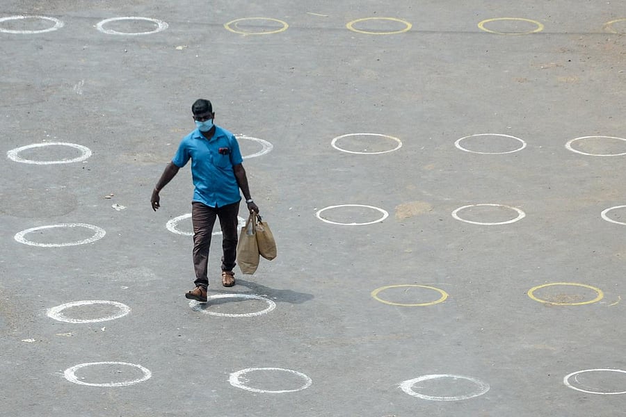 A man carrying bags walks in an area with circles marked on the floor for social distancing at a temporary market set up at a bus stand during a government-imposed nationwide lockdown as a preventive measure against the COVID-19 coronavirus, in Chennai on April 7, 2020. Credit: AFP Photo