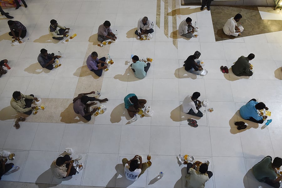 Migrant workers maintain social distance as they sit to eat their meals inside a shopping mall, which is converted into a shelter home during the nationwide lockdown, in wake of the coronavirus pandemic. (PTI Photo)