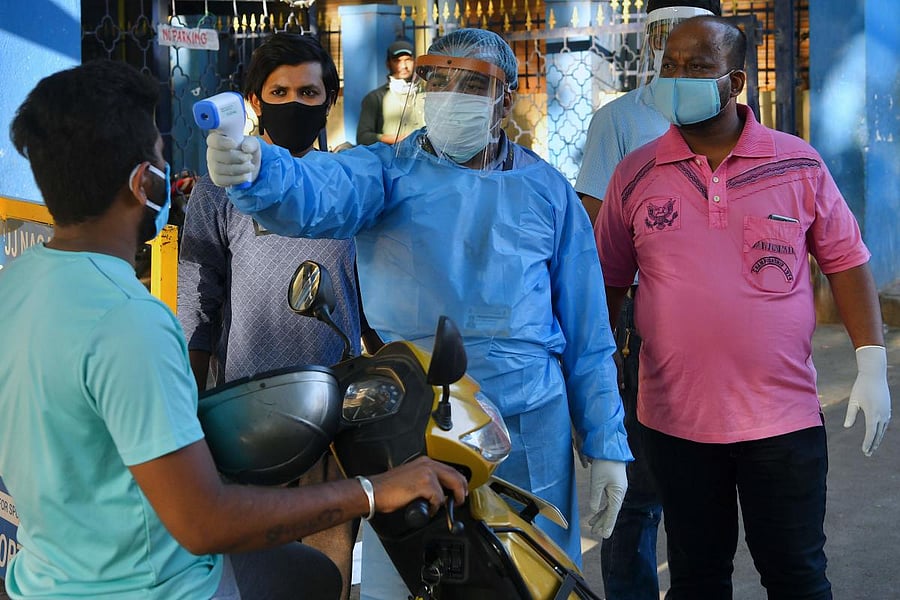 Health officials make enquires and check the temperature of commuters on a road close to a sealed down hotspot during the government-imposed nationwide lockdown against the spread of COVID-19 coronavirus, in Bangalore on April 13, 2020. (Photo by Manjunath Kiran / AFP)