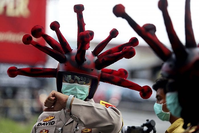 An Indonesian police officer wearing a helmet modified to resemble coronavirus checks his watch during a campaign to promote awareness of the virus outbreak, on a street in Mojokerto, East Java, Indonesia. (AP Photo)