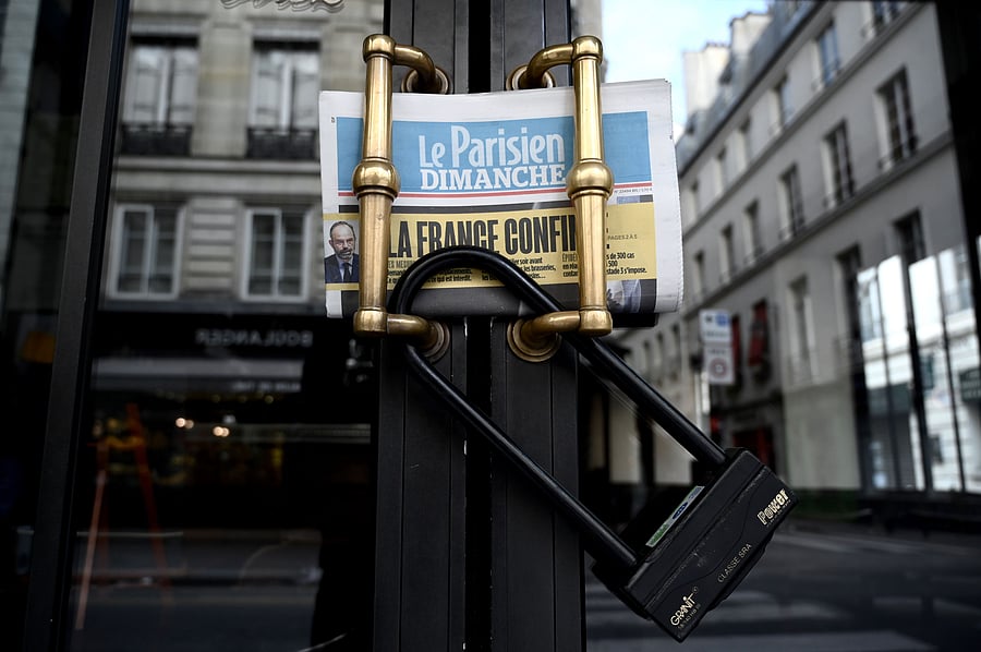 A picture taken on March 15, 2020 in Paris shows the closed entrance door of a cafe and the Parisien daily newspaper reading "France confined" (Credit: AFP)