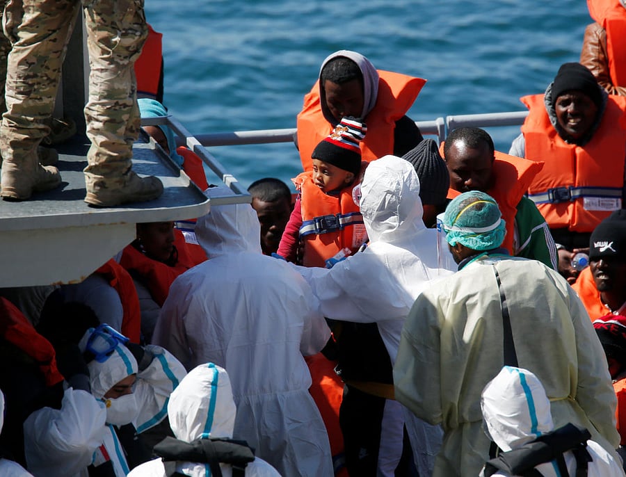 Police officers in protective clothing against possible coronavirus infection tag a child migrant on a military ship after arriving in Senglea. Reuters