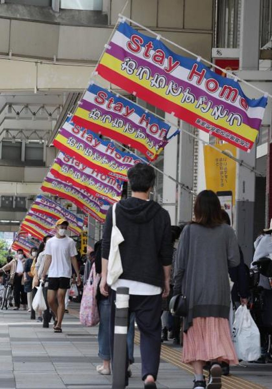 People walk in a street decorated with "Stay Home" flags as a preventive measure against the COVID-19 coronavirus in Tokyo on May 10, 2020. (Photo by AFP)