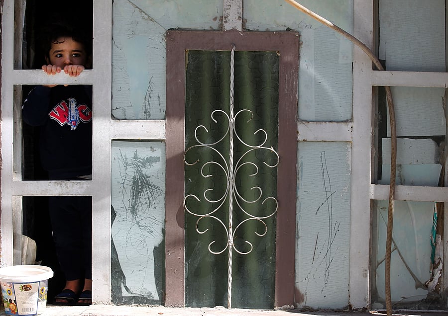 A child looks out of a window as Iraqi public hospital specialised doctors gather in a street before testing residents for COVID-19 in Baghdad's Sadr City/ Representative photo. (Credit: AFP)