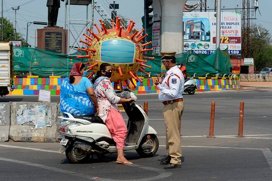 A traffic police officer (R) stands infront of a coronavirus-themed globe at a traffic junction enquire people travel during a government-imposed nationwide lockdown. (AFP Photo)