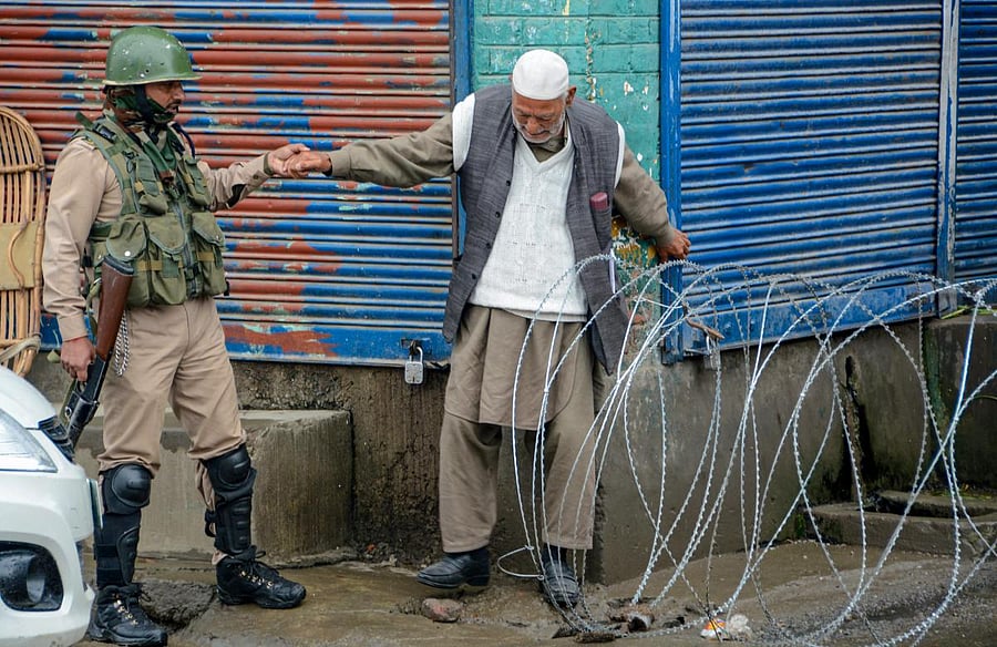 Security person help an elderly man to cross a blocked road during strict curfew imposed to maintain law and order problem following the killing of most wanted militant Zakir Musa, in Srinagar on Friday, May 24, 2019. (PTI Photo)