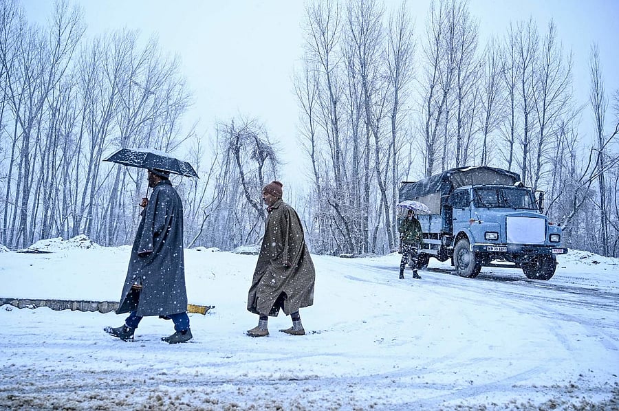 People walk as a security personnel (R) holding an umbrella stands next to a security vehicle near the Dal Lake during a snowfall in Srinagar on January 12, 2020. (AFP Photo)