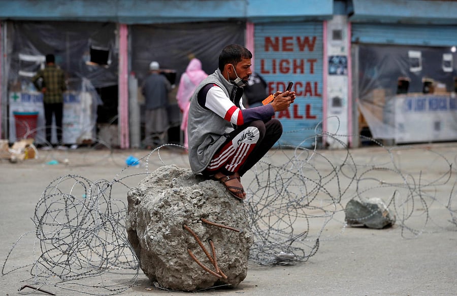 A man checks his mobile phone as he sits on a cement block tied to concertina wire laid across a road in front of pharmacy shops during an extended lockdown to slow the spreading of the coronavirus disease in Srinagar. Reuters