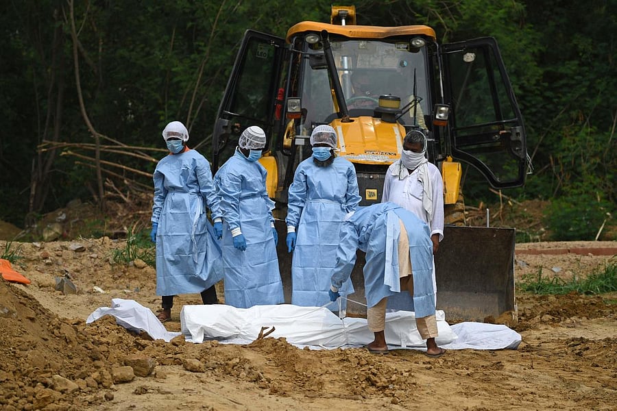 A relative wearing protective gear ties up the body of a victim, who passed away from Covid-19, before the burial at a graveyard in New Delhi. File Photo. Credit: AFP Photo