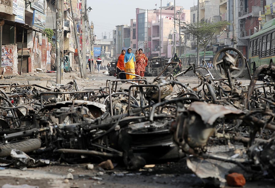 Women walk past charred vehicles in a riot affected area following clashes between people demonstrating for and against a new citizenship law in New Delhi, India, February 27, 2020. Credit: Reuters Photo