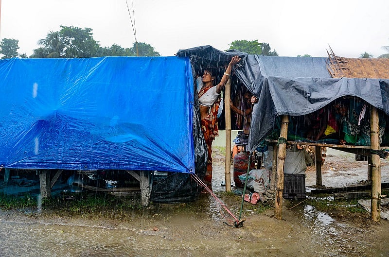 A woman tries to cover her makeshift shelter as it rains, in a flood-hit area of Morigaon. Credits: PTI Photo
