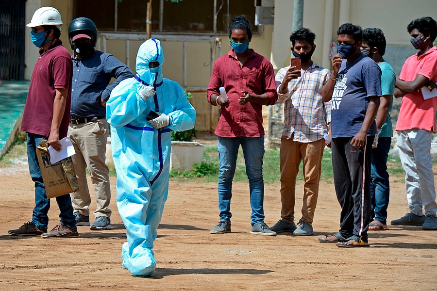 A health worker wearing Personal Protective Equipment (PPE) gear walks past the residents standing in queue to register their names at a free testing centre. Credit: AFP Photo