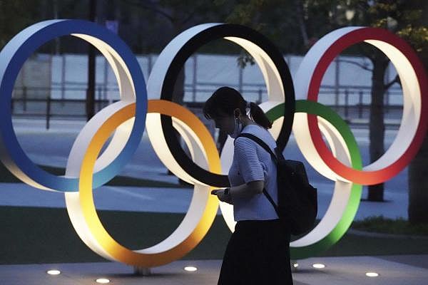 A woman walks at the Olympic rings in front of the New National Stadium in Tokyo. Credit: AP