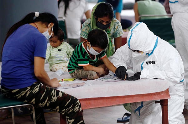 A medical worker helps a boy to draw inside a care centre for the coronavirus disease. Credit: Reuters