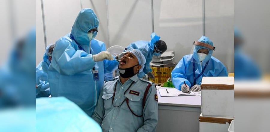 A medical staff wearing a Personal Protective Equipment (PPE) suit (L) takes a swab sample from a man in Delhi. Credit: AFP Photo