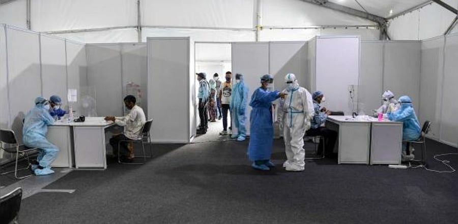 Medical staff wearing Personal Protective Equipment (PPE) suits write down the details of people before taking samples. Representative Photo. Credit: AFP