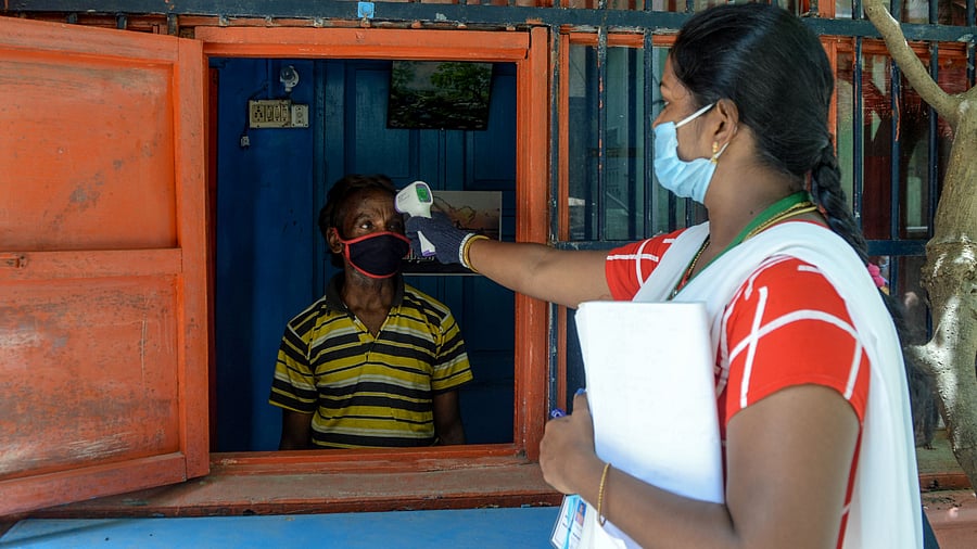 A health worker (R) checks the body temperature of a man at a containment zone implemented as a preventive measure against the Covid-19. Credits: AFP Photo