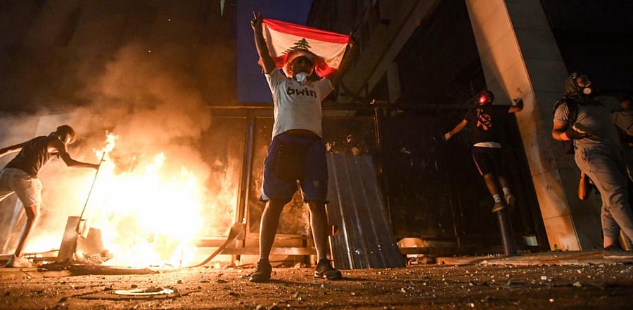 A Lebanese protester lifts the national flag next to a fire lit by demonstrators amid clashes with security forces in downtown Beirut