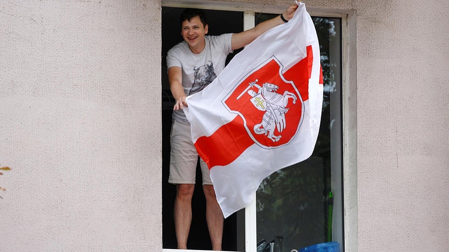 An opposition supporter waves a flag while leaning out of a window of an apartment block during a rally held by employees of Minsk Tractor Works, who protest against presidential election results and demand re-election in Minsk. Credit: Reuters