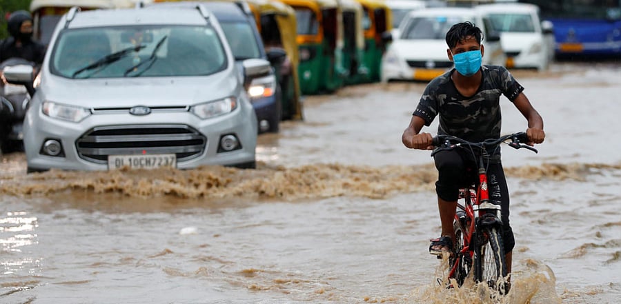A boy wearing a protective mask rides a bicycle through a flooded street during heavy rains in New Delhi. Credit: Reuters