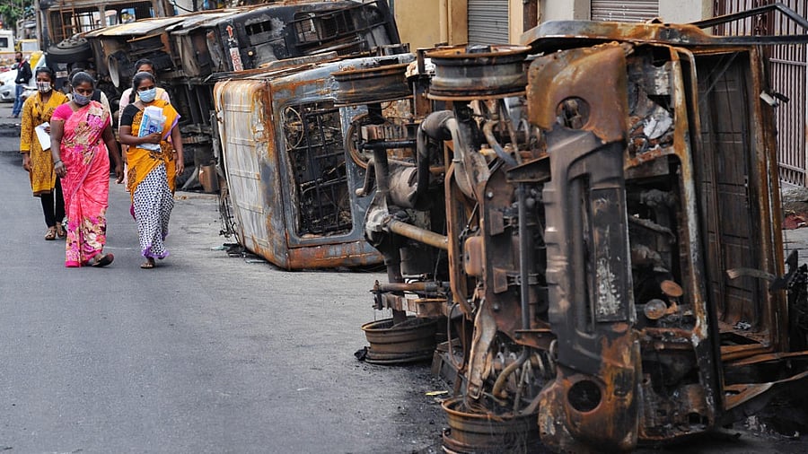 Women walk past charred vehicles in DJ Halli, Bengaluru, on Tuesday. DH PHOTO/PUSHKAR V