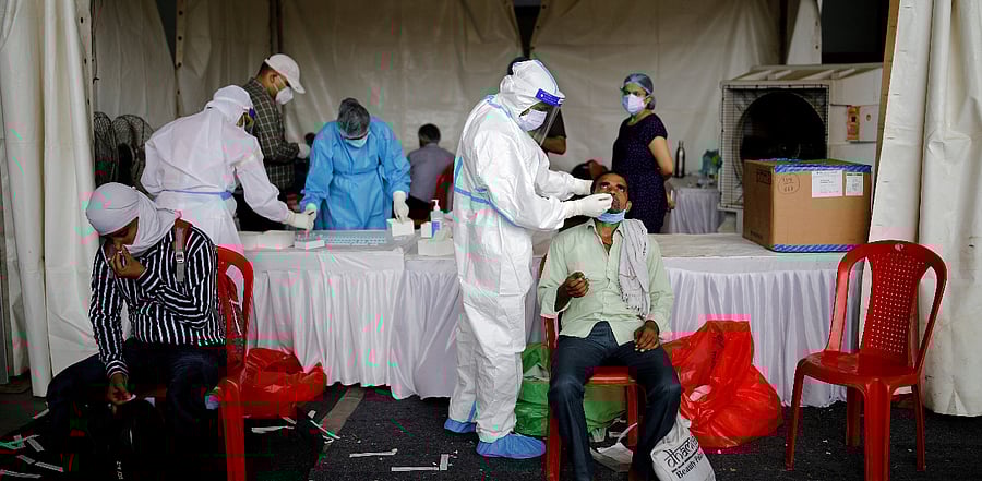 A healthcare worker wearing personal protective equipment (PPE) takes a swab from a migrant worker, who returned to Delhi from his native state. Credit: Reuters File Photo