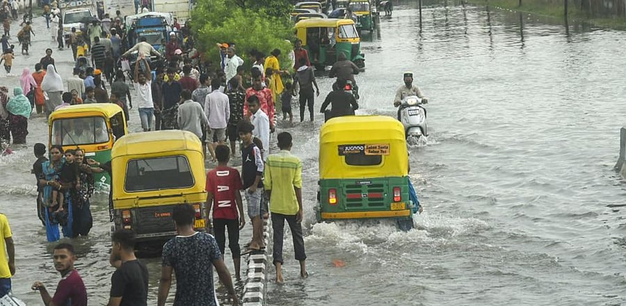 Commuters wade through a waterlogged street during heavy rains. Credit: PTI